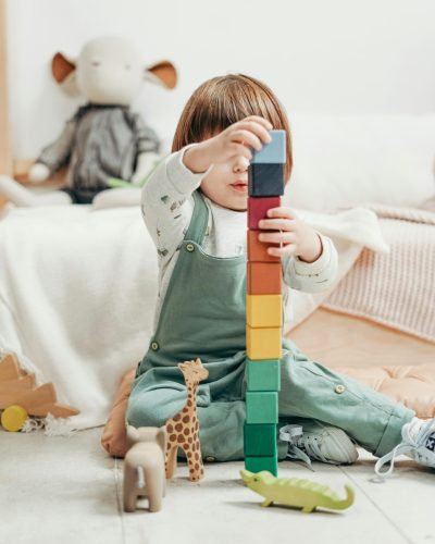 A cute child stacks colorful wooden blocks while playing indoors, surrounded by toys.