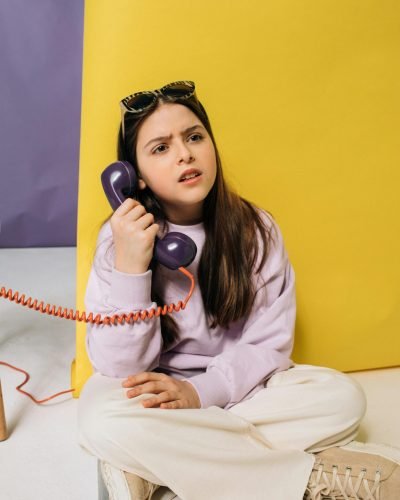 A young girl expressing confusion while talking on a retro phone against a colorful background.